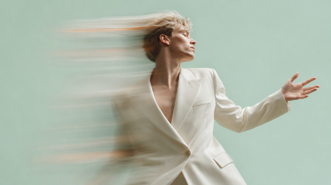 A person mid-turn in a mint-green studio, one arm outstretched gesturing toward an unseen wall of concepts, wearing a structured cream blazer, shot