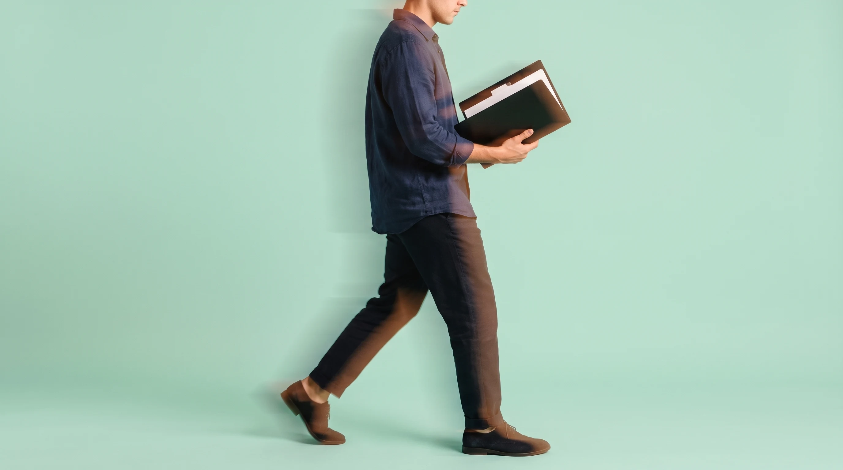 Person mid-step across a mint-backdrop studio, profile framing, holding an open unbranded portfolio binder, wearing a relaxed navy linen shirt