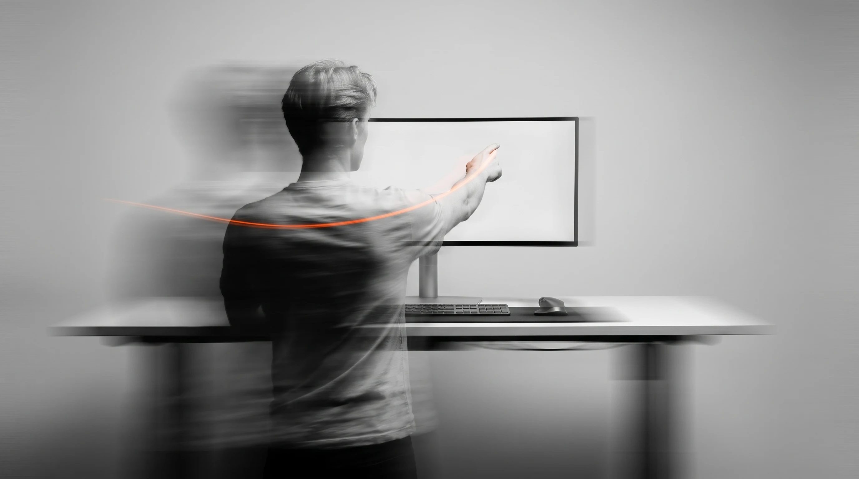 A person mid-turn at a standing edit desk, one hand raised in a pointing gesture toward a blank widescreen monitor, viewed in profile from behind