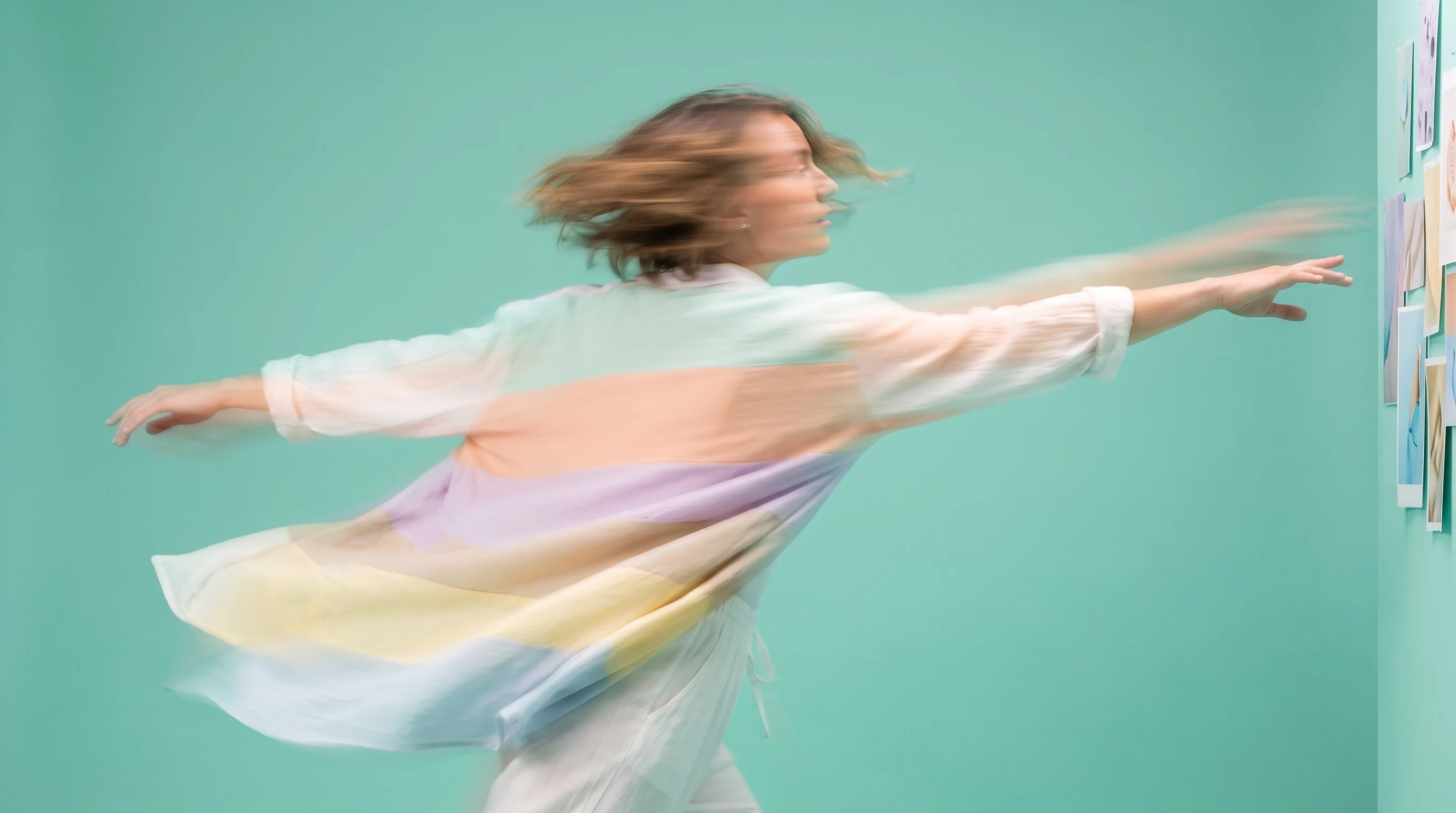 A person mid-turn in a mint studio, arms outstretched gesturing at an off-frame wall of printed moodboard grids, shot three-quarter from the front
