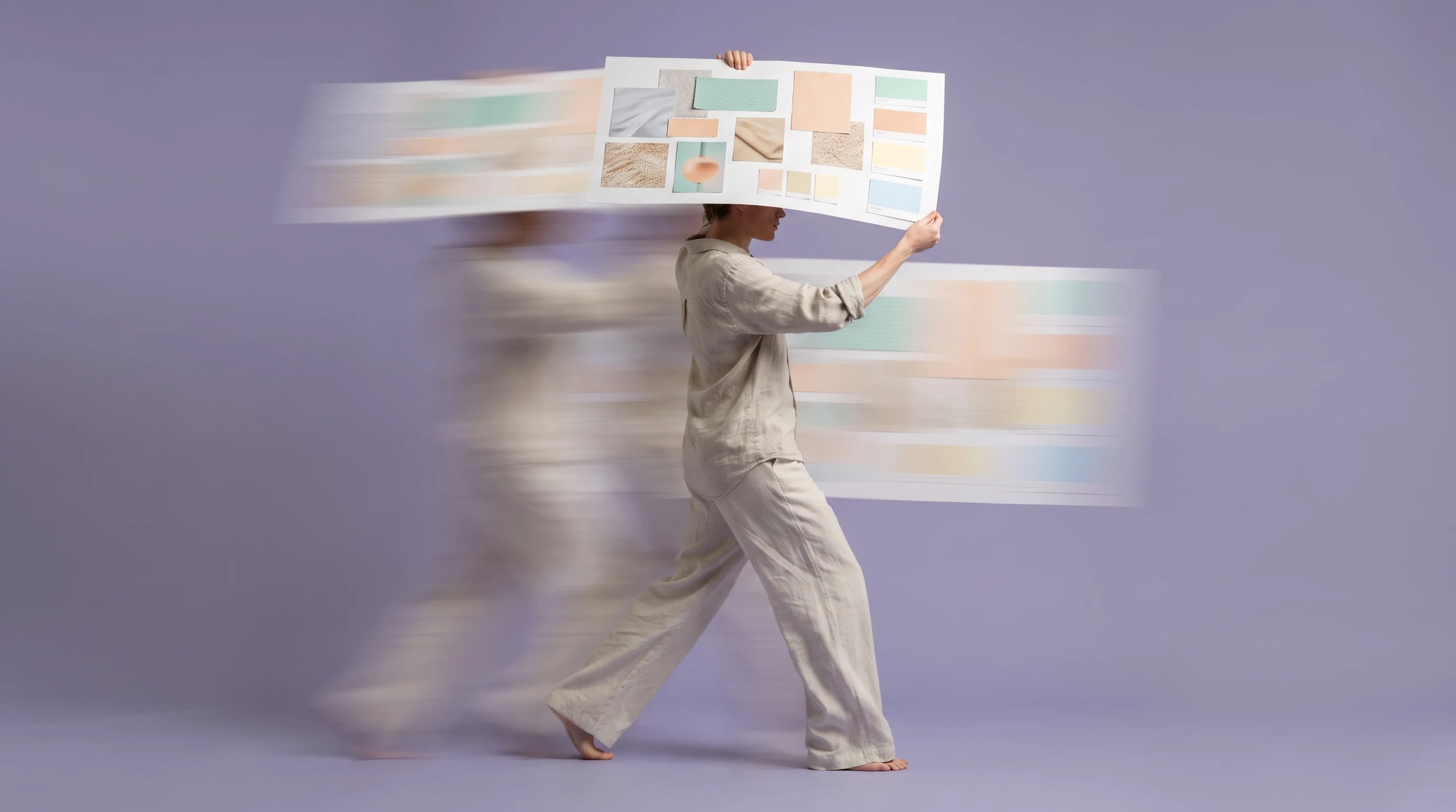 A person mid-step across a lilac-backdrop studio, holding a large unbranded mood-board sheet overhead with both hands, profile framing, relaxed linen