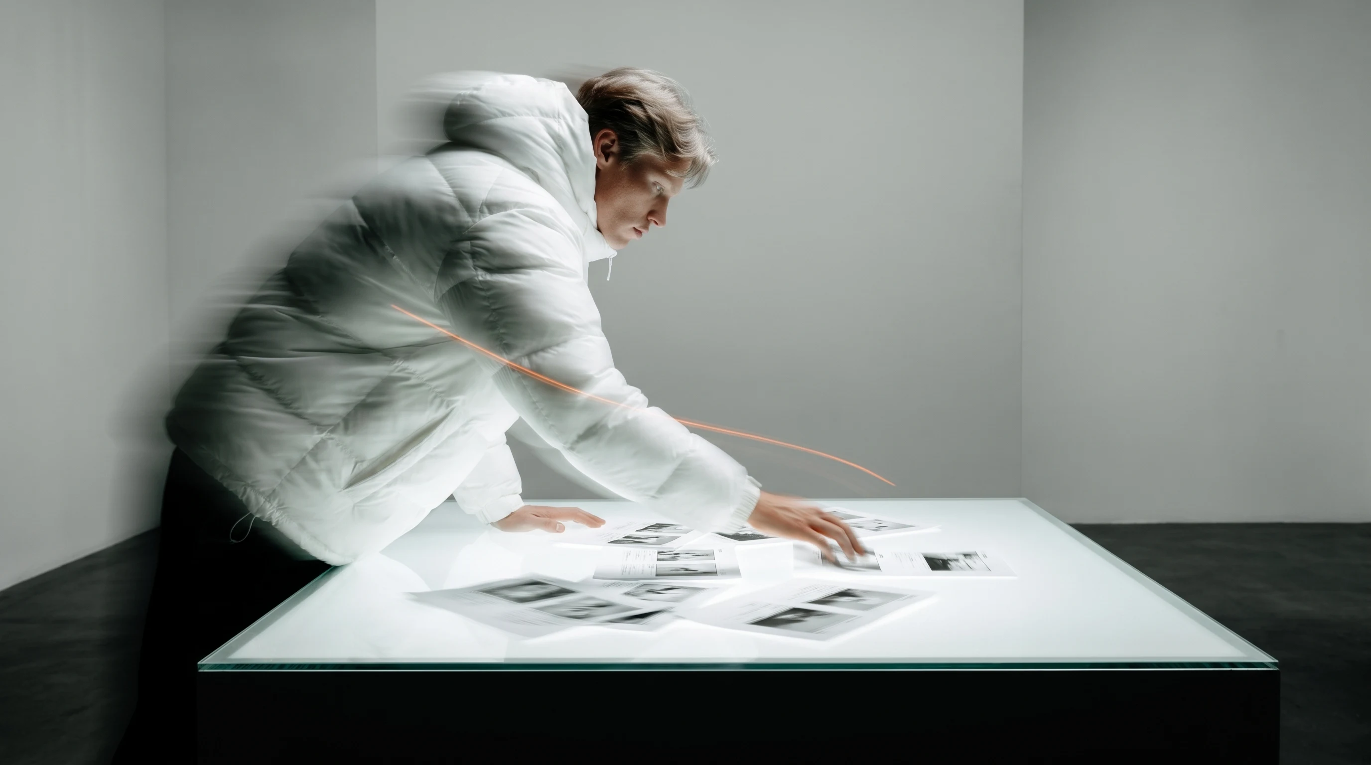 A creative director mid-lean over scattered unbranded storyboard frames spread across a large light table, reaching forward, side profile
