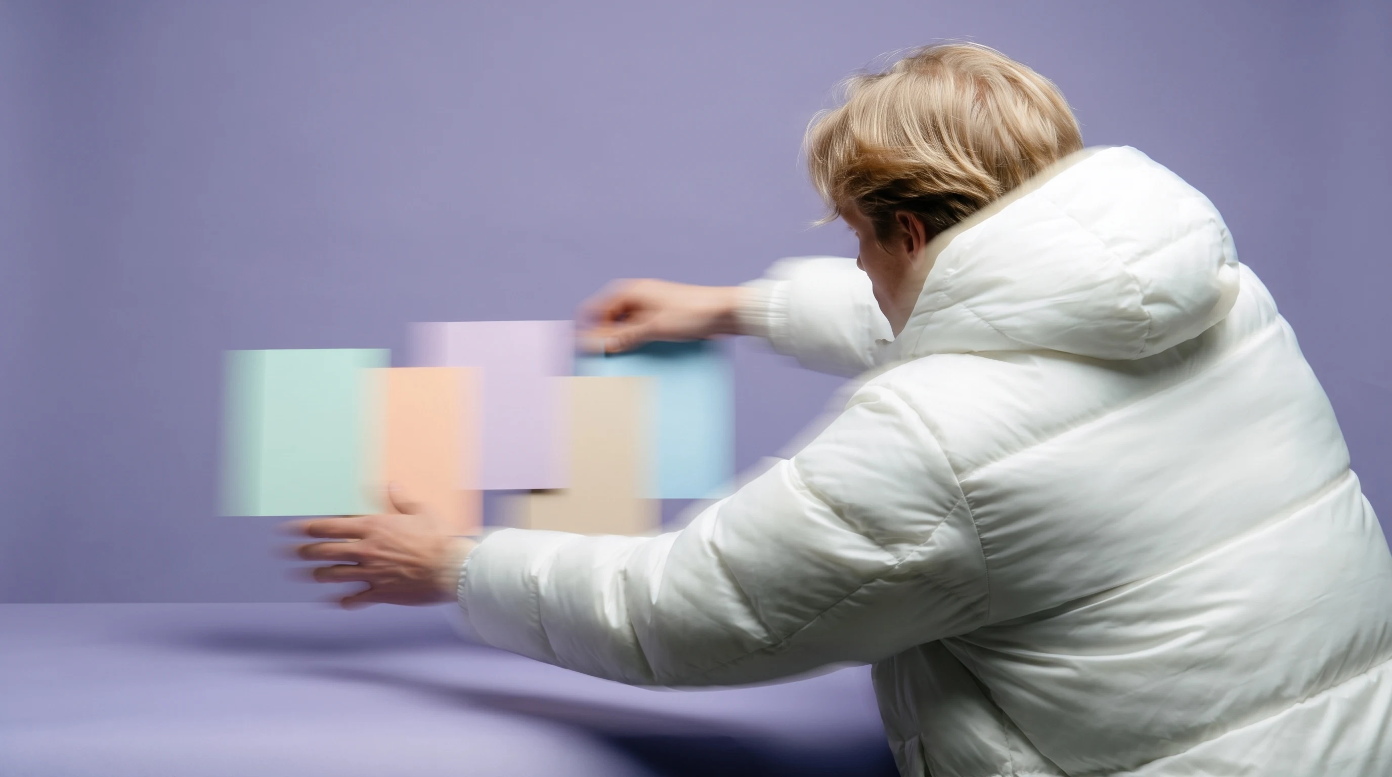 A person mid-reach repositioning a stack of unbranded flat-lay cards across a clean content-styling table, shot from behind, lilac backdrop