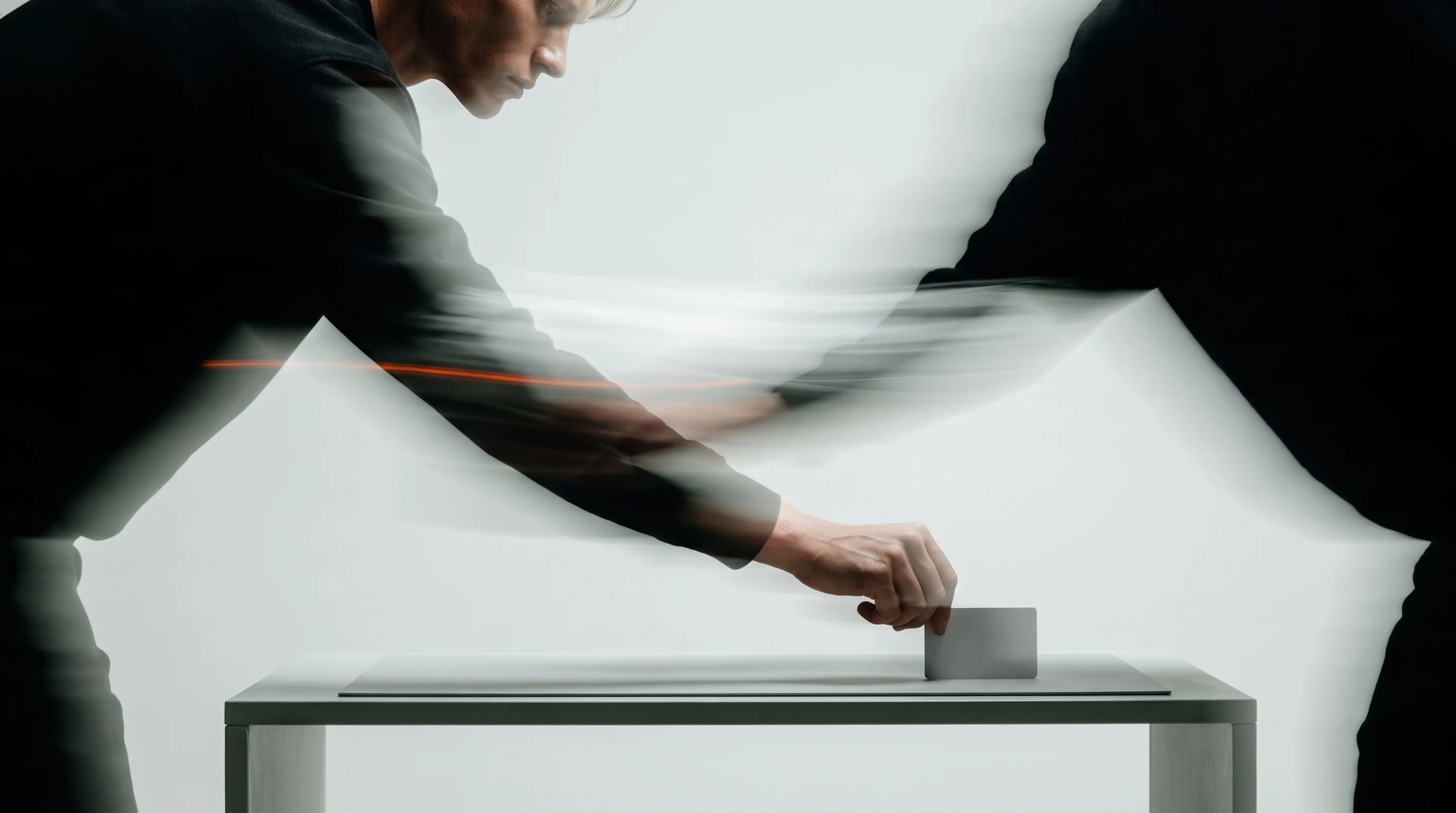 A person mid-lean forward over a low table, arm outstretched placing an unbranded blank card on a flat surface, framed tight from the side,