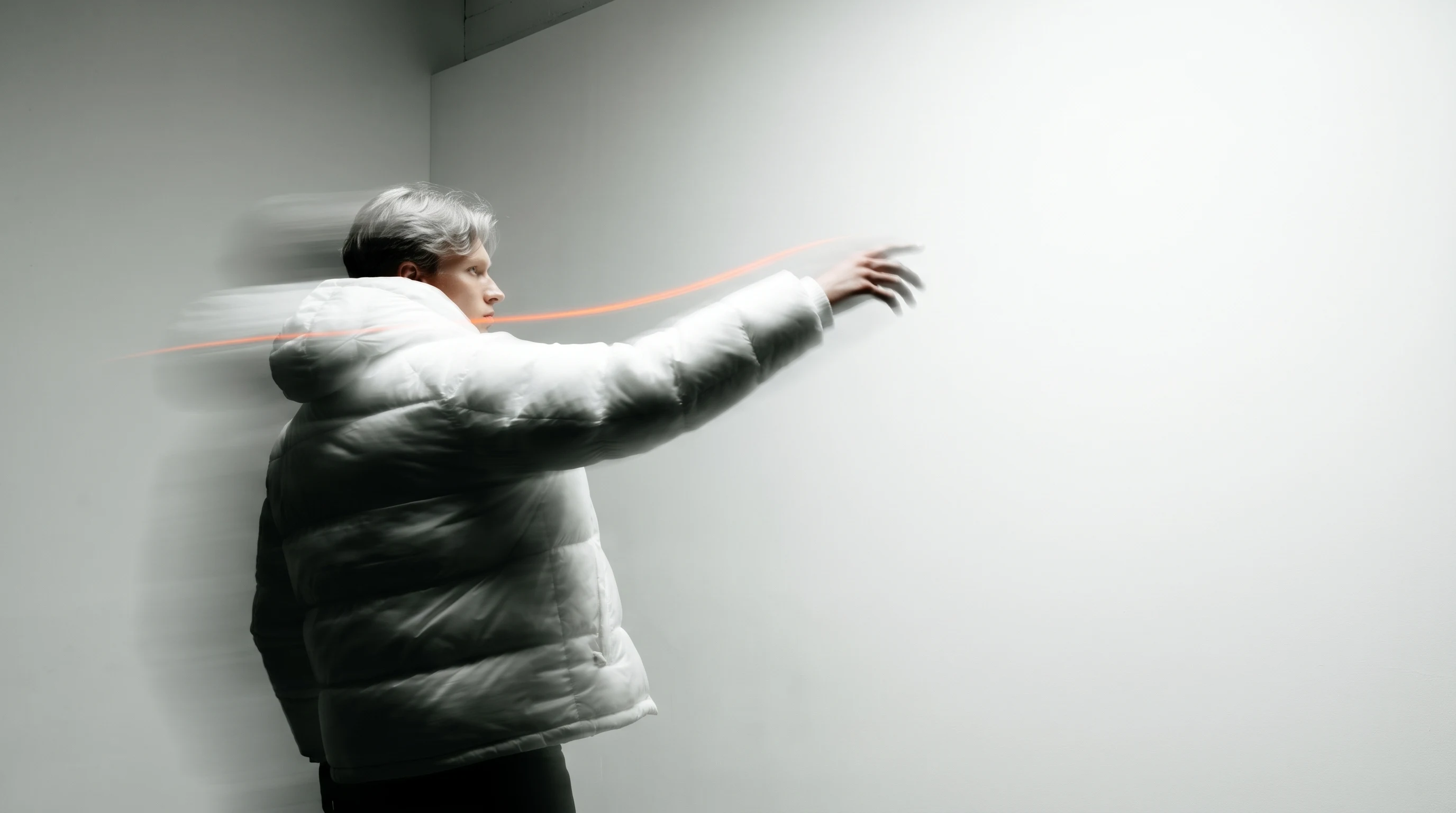 A person mid-spin in a sparse studio space, one arm gesturing decisively toward a bare white wall, three-quarter framing from slightly below,