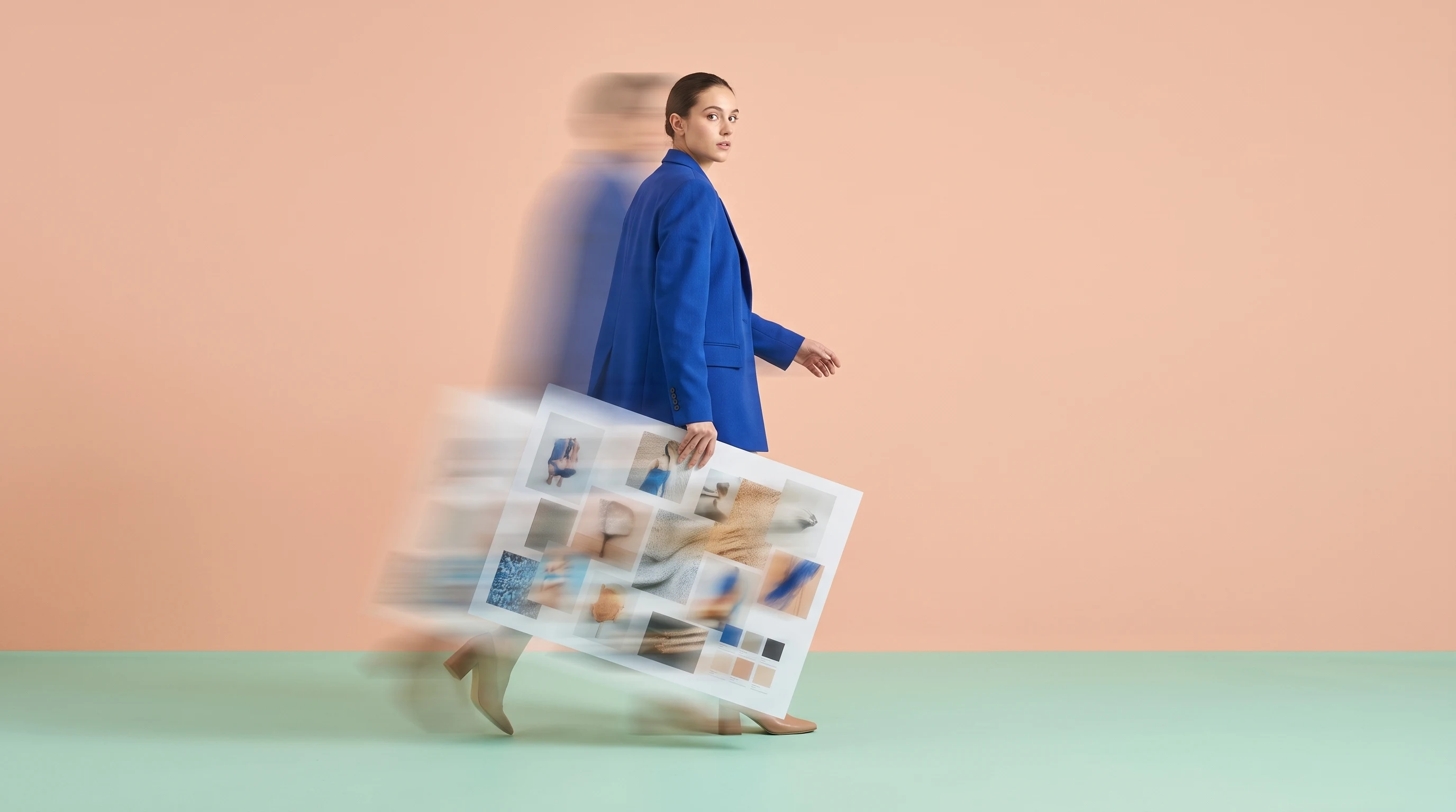 a person mid-step across a mint-green studio floor, carrying a large unbranded printed mood-board sheet under one arm, glancing back over their