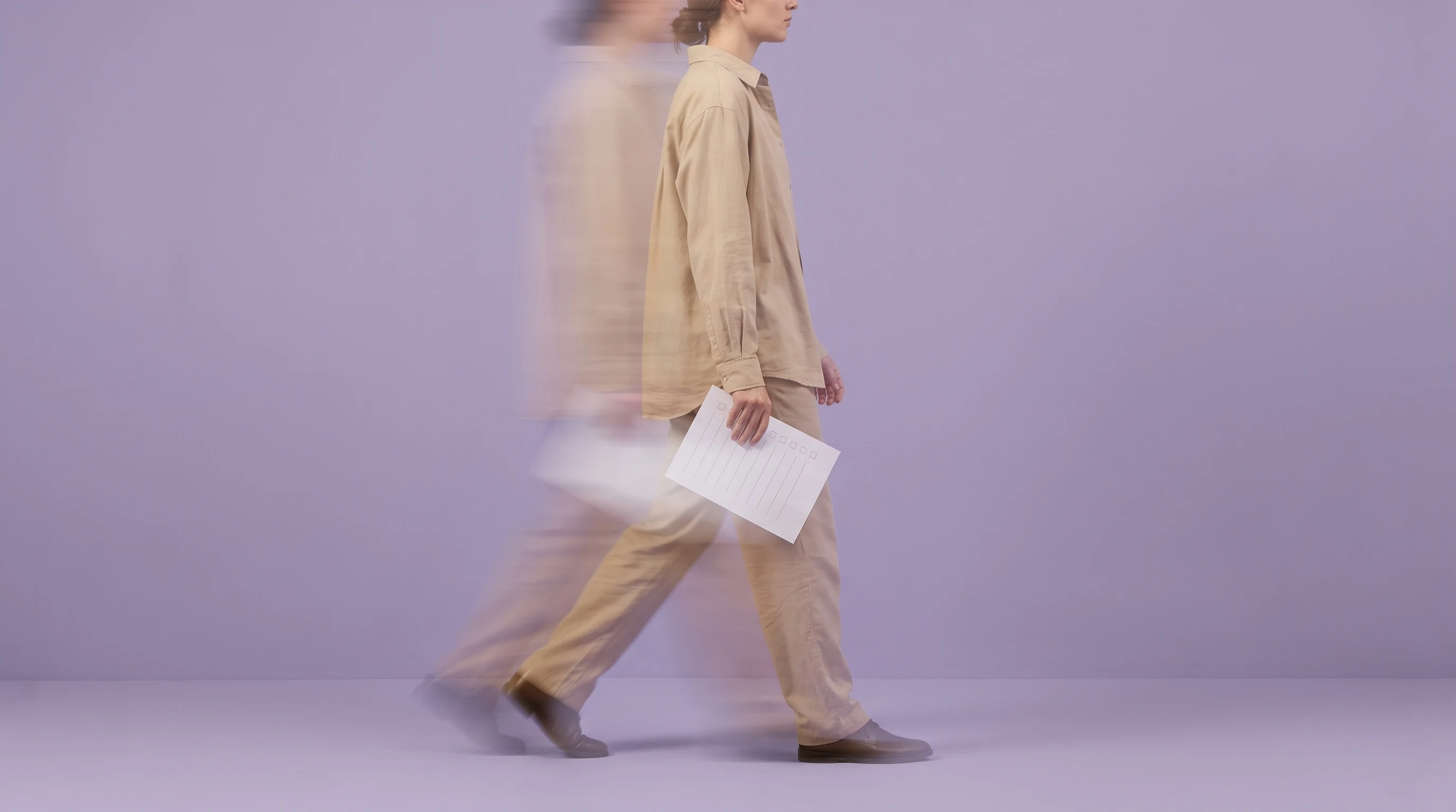 a person mid-step across a lilac studio backdrop, holding a printed checklist sheet face-down at their side, wearing a sand-coloured shirt, framed