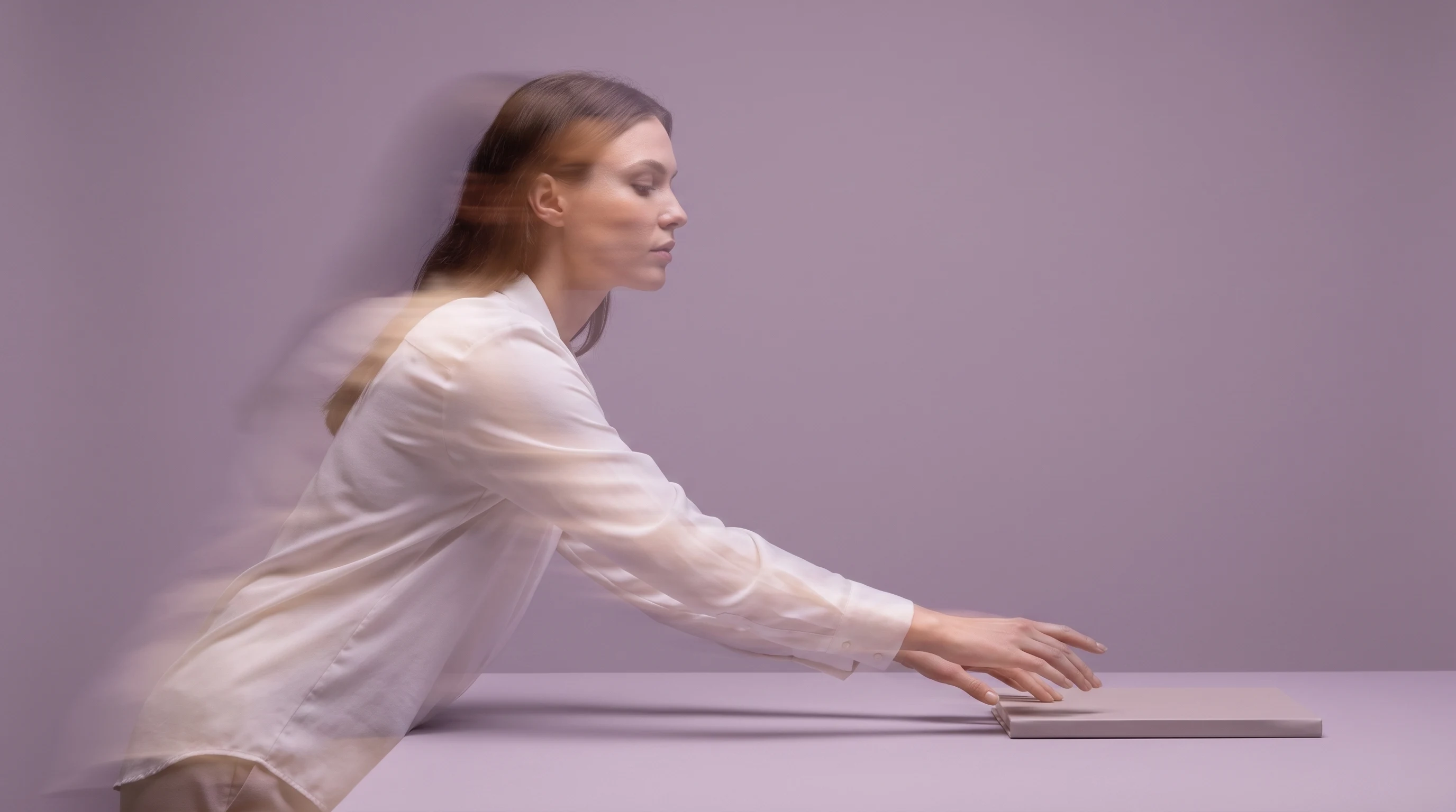 A woman mid-reach toward an unbranded flat object on a waist-high surface, lilac backdrop, wearing a soft white shirt, three-quarter low-angle framing