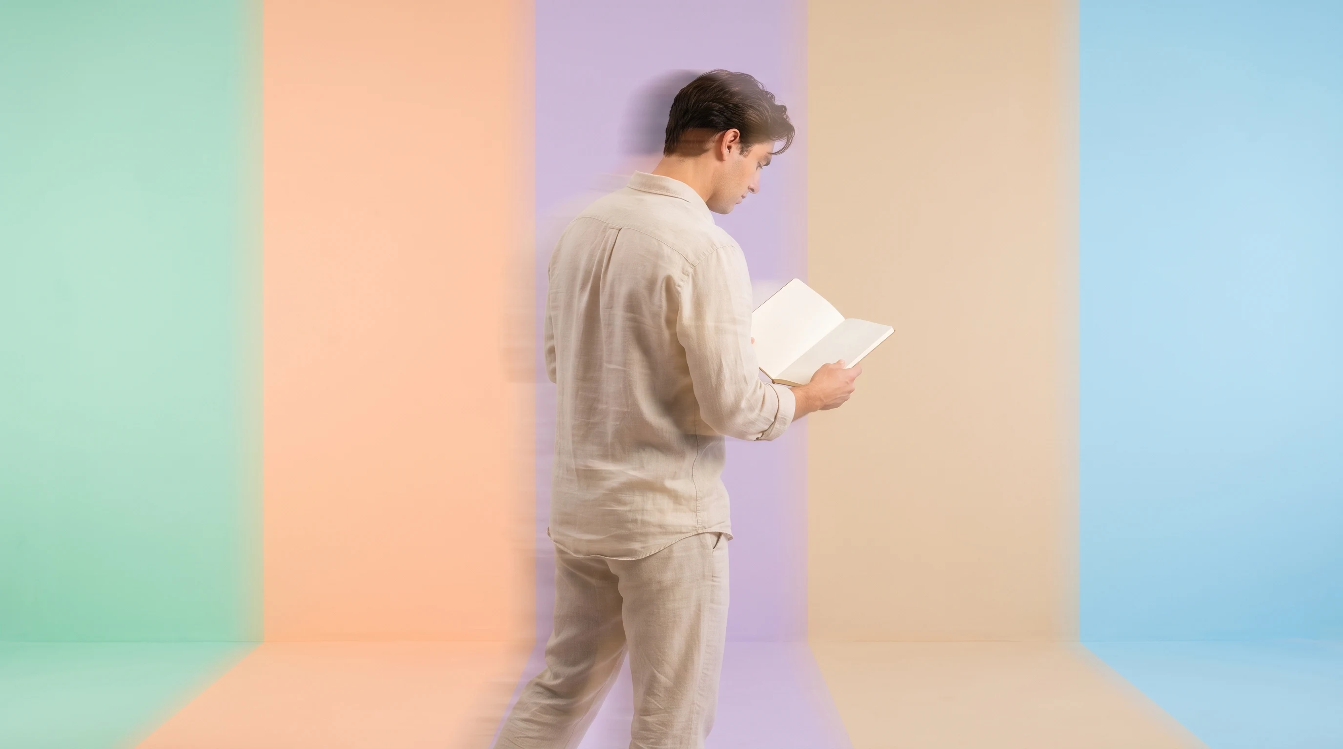 A person in a linen shirt mid-step across a mint-green studio, glancing down at an open unbranded notebook held at waist height, three-quarter