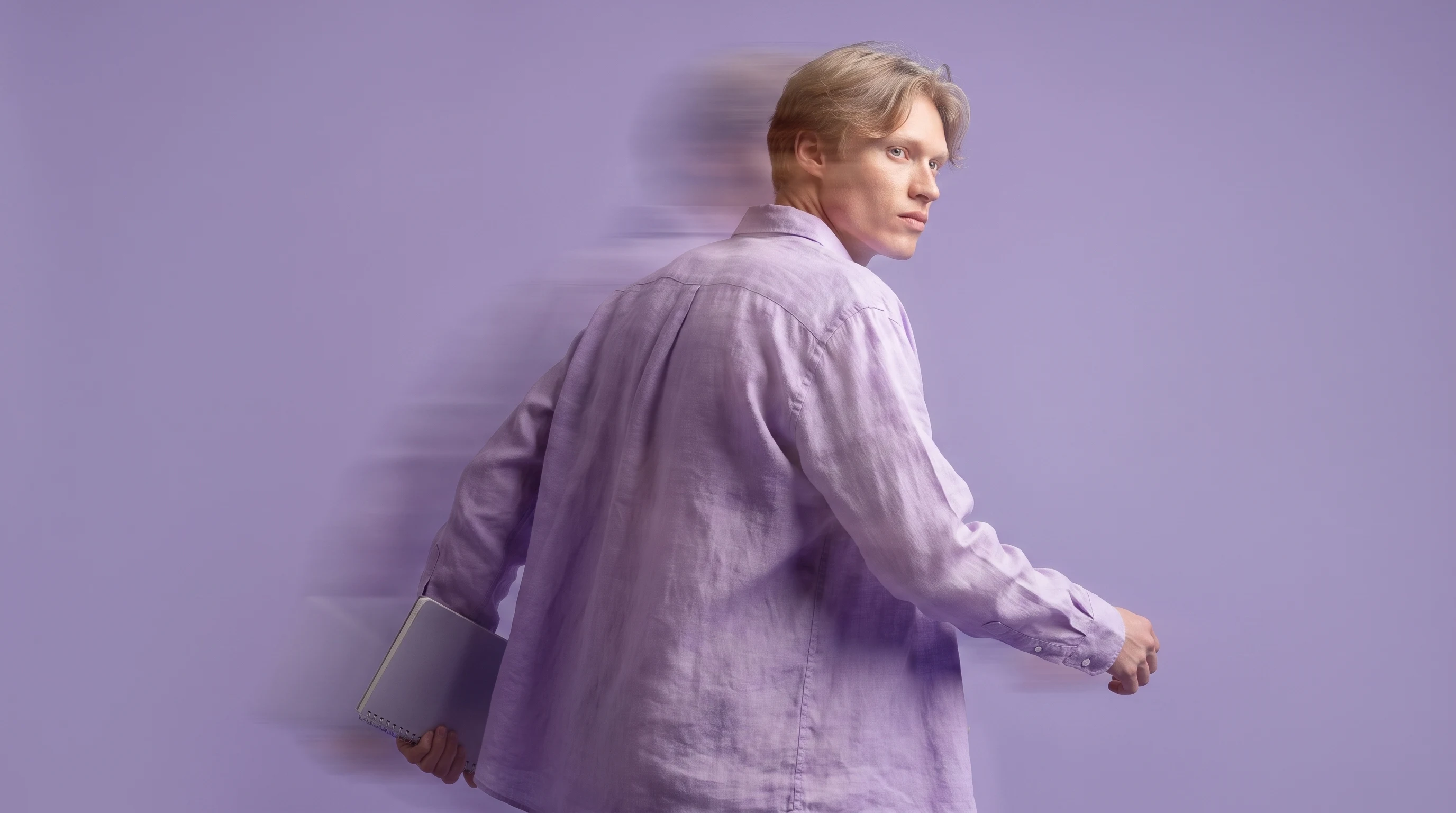 A person mid-step in a lilac studio, glancing back over one shoulder, slim notebook tucked under their arm, wearing a relaxed linen shirt, profile