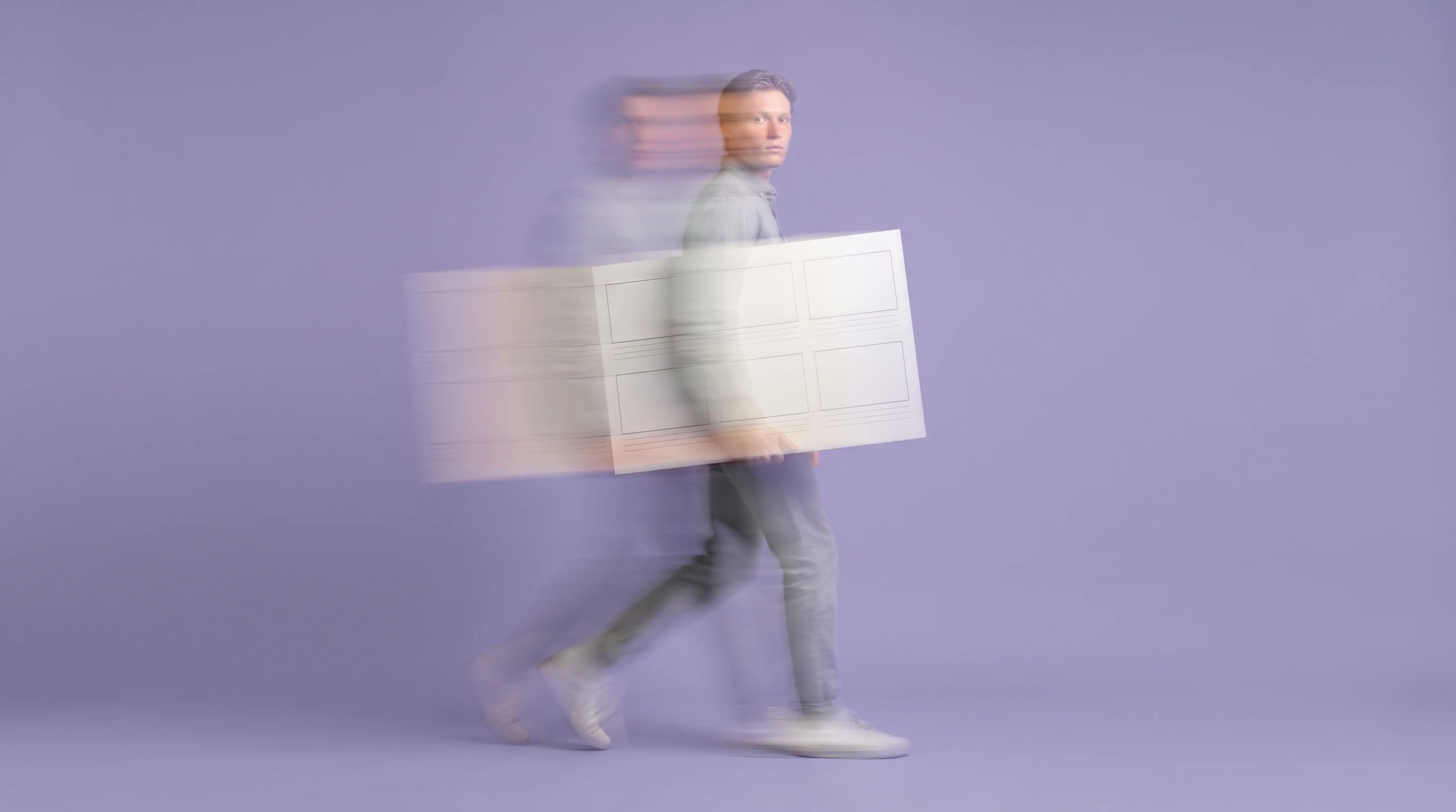 A person mid-step in a lilac studio, holding a large unbranded storyboard panel at chest height, profile framing, looking toward camera