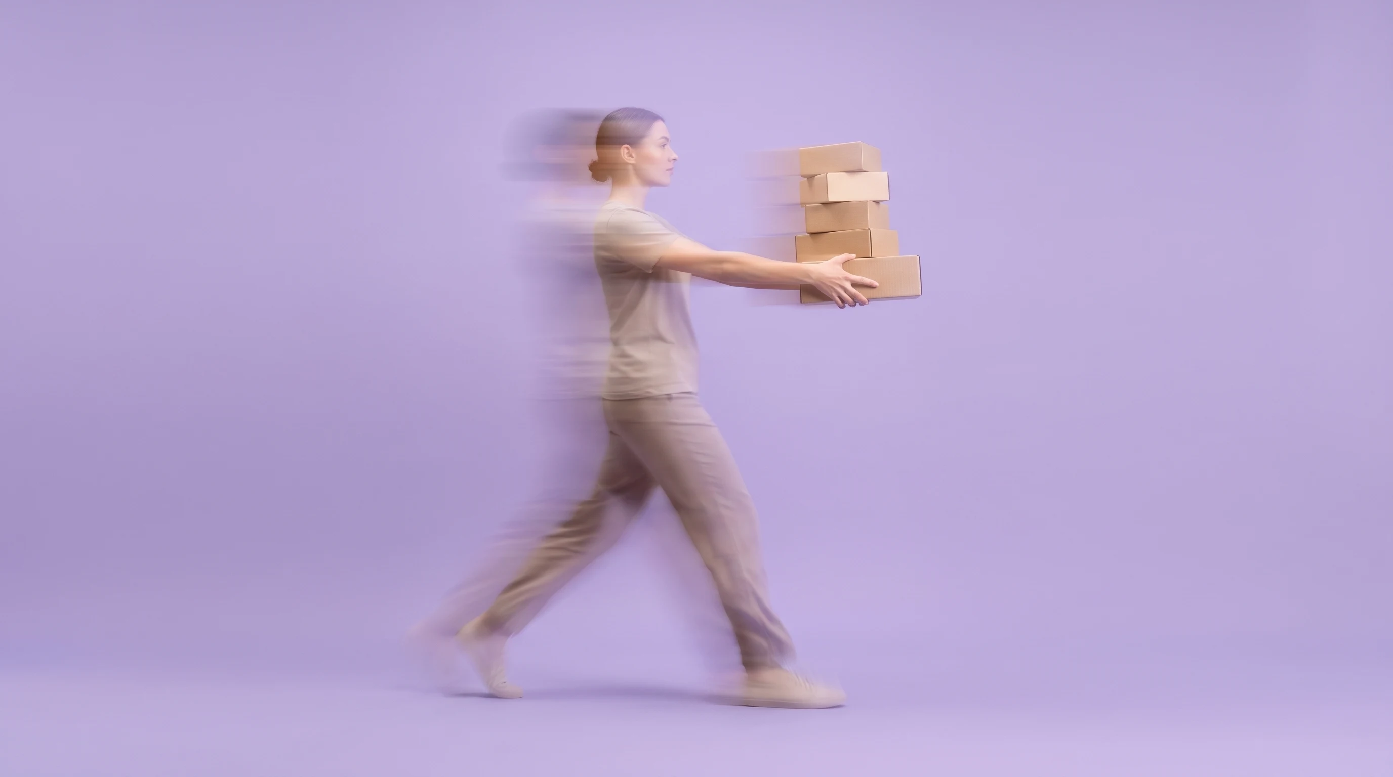 A person mid-step in a lilac-backdrop studio, arms extended carrying a stack of small unbranded product boxes at chest height, three-quarter view,