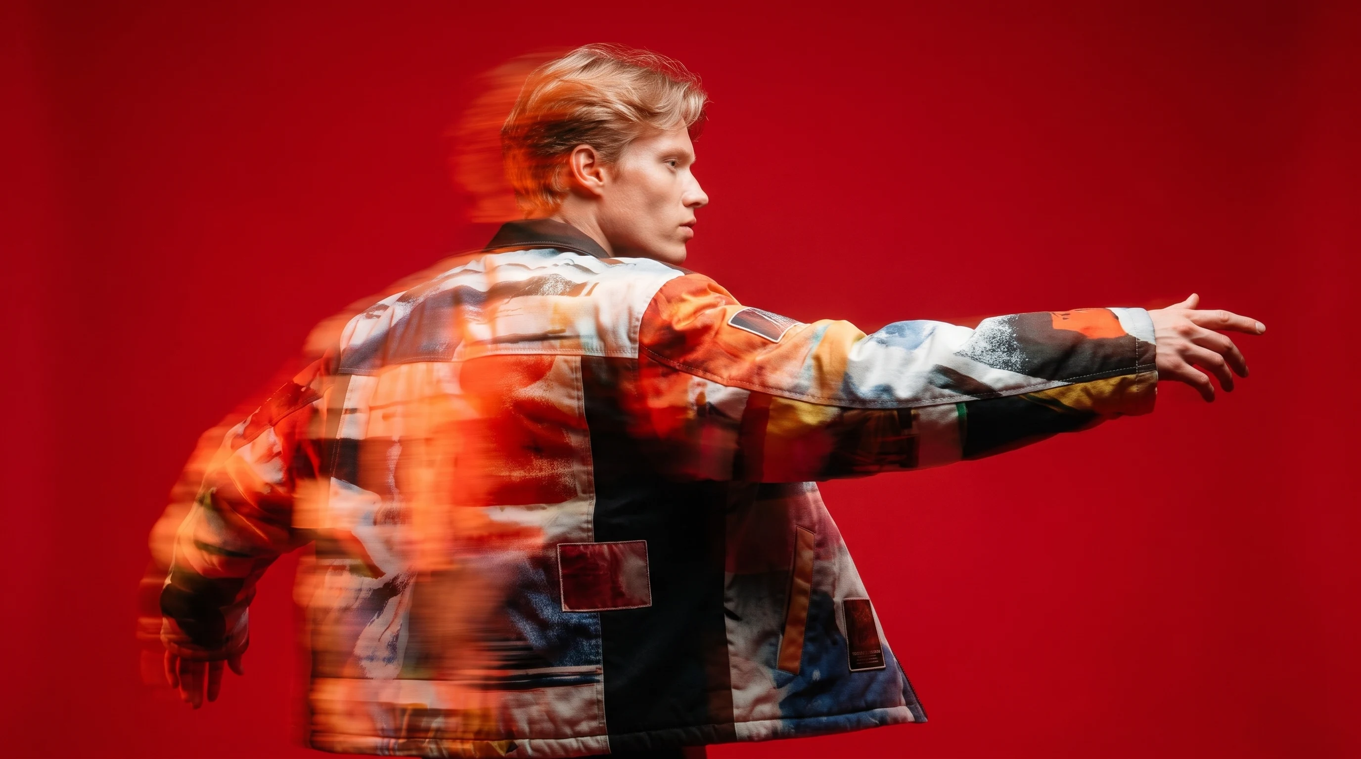 A person mid-spin in a studio, arm outstretched directing an invisible camera, profile framing, wearing an oversized creative-director jacket