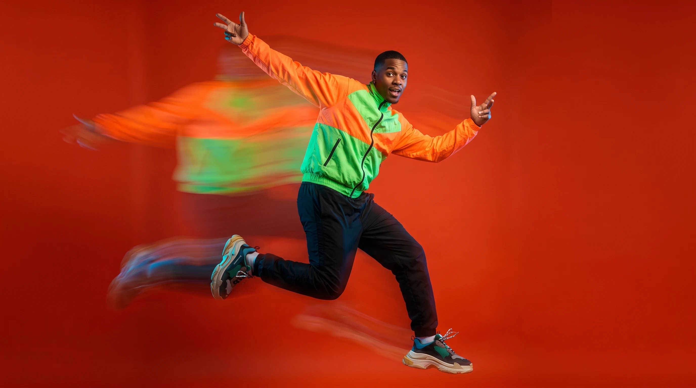 A person mid-leap in a studio, arms raised wide, three-quarter front view, wearing athletic-inspired streetwear, pitching a sports broadcast concept