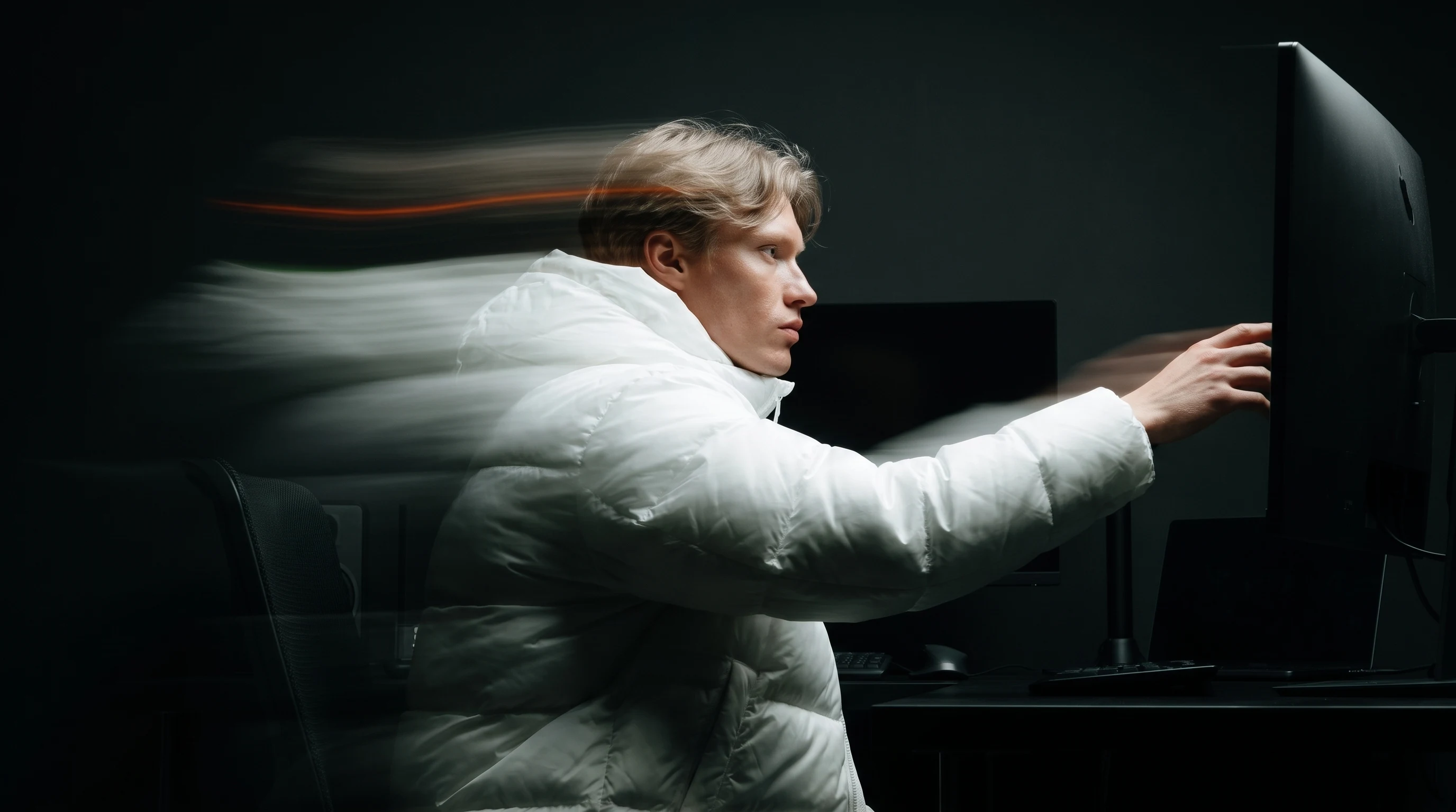 a person mid-turn in a dark edit suite, one arm reaching toward a large monitor just out of frame, caught in three-quarter profile, soft light raking