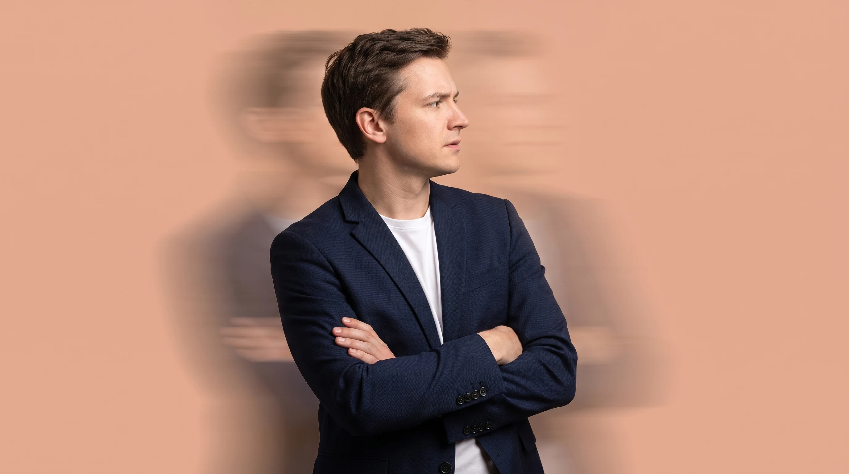a person mid-turn in profile, arms crossed loosely at chest height in a sceptical evaluating stance, looking slightly off-frame, peach studio