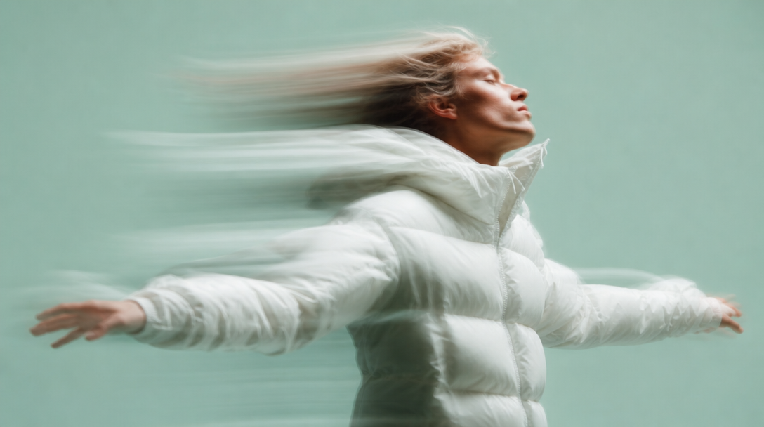 A person mid-turn in a mint-backdrop studio, arms extending outward as if arranging an invisible scene, three-quarter framing from slightly below eye